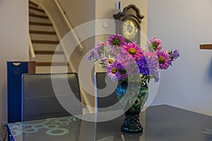 Beautiful view of green vase with colorful asters on grey glass table.