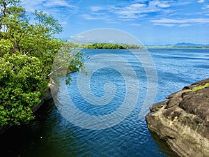 A beautiful view of a lake with rock area and trees and cloudy blue sky