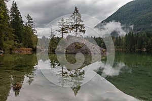 Beautiful view of a lake with a rock in it and mountains in the background in foggy weather.