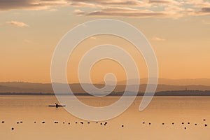 Beautiful view of a lake at sunset, with orange tones, birds on water and a man on a canoe