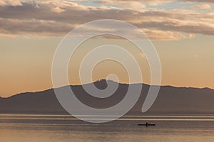 Beautiful view of a lake at sunset, with orange tones, birds on water and a man on a canoe