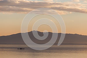 Beautiful view of a lake at sunset, with orange tones, birds on water and a man on a canoe