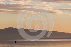 Beautiful view of a lake at sunset, with orange tones, birds on water and a man on a canoe