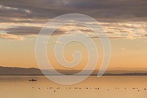 Beautiful view of a lake at sunset, with orange tones, birds on water and a man on a canoe