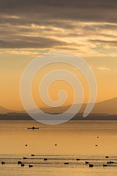 Beautiful view of a lake at sunset, with orange tones, birds on water and a man on a canoe