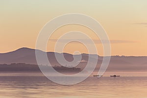 Beautiful view of a lake at sunset, with orange tones and two men on canoes