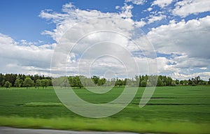 Beautiful view of landscape with green fields, green forest trees and blue sky with white clouds.