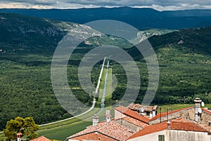 A beautiful view of the long road leading from the town with red tiled roofs far away to the horizon with green hills.