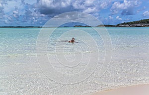 Beautiful view of man floating in Atlantic ocean on sandbar with white sand at low tide in Bahamas islands