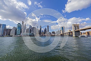 Beautiful view of Manhattan skyscrapers from Hudson River with Brooklyn bridge on backdrop blue sky with white clouds.