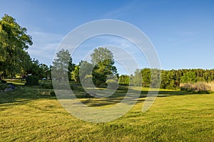 Beautiful view of mown meadows in rural countryside near the lake against the backdrop of the forest on a warm sunny day.