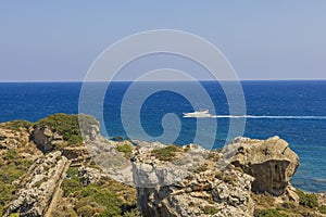 Beautiful view of natural landscape with passing sailing yacht on rocky coastline on endless surface of blue sea water on horizon.