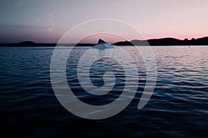 Beautiful view of an ocean with an iceberg in it against a shore in the sunset