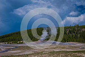 Beautiful view of old faithful Geyser Basin located in Yellowstone National Park, surrounded by vapor with a green