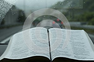 Beautiful view of open Holy Bible in Psalm 121 on stormy day. Blurred background with expressway and cars.