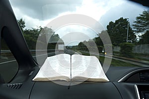 Beautiful view of open Holy Bible in Psalm 91. Windshield with raindrops. Blurred background with expressway and cars.