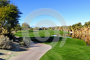 A beautiful view of a par 5 with the desert surrounding the hole as well as a pond. The golf course is in Palm Springs photo