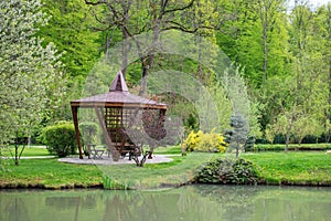 The beautiful view of the park with the trees, green grass field ,gazebo and the pond on background of blue sky. Spring