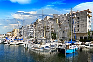 Beautiful view of the pier with boats, yachts, boats and a high-rise building against the blue sky in the Empuriabrava city