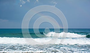 Beautiful view of the raibow over the sea and waves braking on the shore