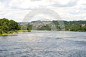 A beautiful view of the River Rhine in West Germany on which a transport barge flows, there are houses on the hill and people bath