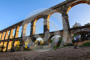 Beautiful view of roman Aqueduct Pont del Diable in Tarragona at sunset with people jogging in front of it