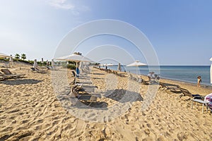 Beautiful view of sandy beach. Parents with children rest under white umbrellas against blue sky.