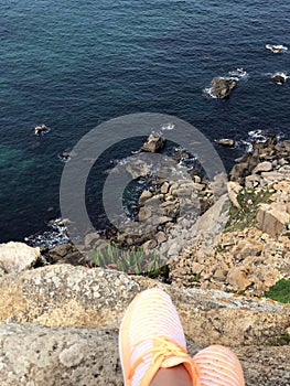 Beautiful view: sea, rocks, stones at the foot of a girl in orange sneakers.