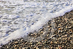 A beautiful view of sea waves on pebbles. Background of foam and stones.