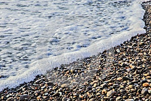 A beautiful view of sea waves on pebbles. Background of foam and stones.