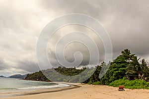 Beautiful view of Seychelles beach with a single chair in the sand on a cloudy warm day. Concept of tourist islands