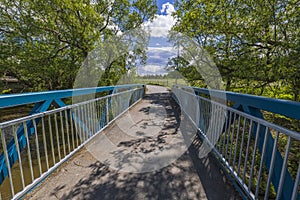 Beautiful view of small bride over river on green trees and blue sky with white clouds background.