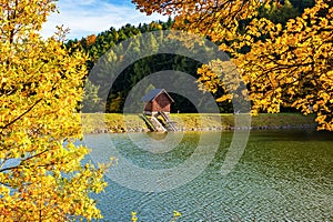 Beautiful view of small wooden house on bank of lake near forest during autumn