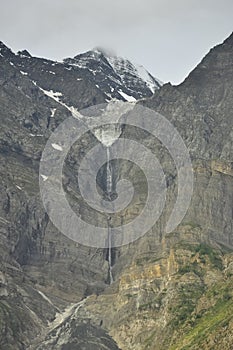 Beautiful view of snow melting and water falling down from top of rocky mountain during cloudy weather