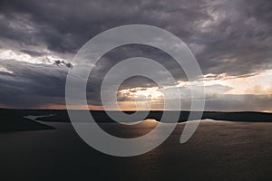 Beautiful view of sun rays from dark clouds above lake. Sunset light over hill and river landscape. Dramatic moody scenery. Bakota