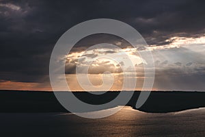 Beautiful view of sun rays from dark clouds above lake. Sunset light over hill and river landscape. Dramatic moody scenery. Bakota