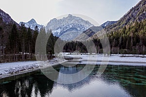 Beautiful view at sunset of the peaceful lake Fucine Tarvisio, Italy with green forest and snowy mountains in the