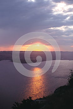 Beautiful view of sunset warm light from dark clouds above lake. Sunny rays over hill and river landscape. Dramatic moody scenery