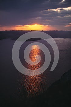 Beautiful view of sunset warm light from dark clouds above lake. Sunny rays over hill and river landscape. Dramatic moody scenery