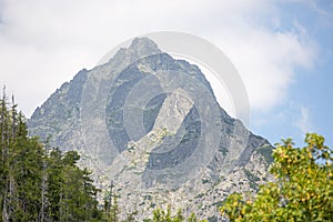 Beautiful view of a tall peak standing proud, overlooking vibrant green trees in High Tatras