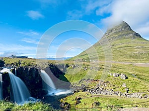 Beautiful view to mountain Kirkjufell and Kirkjufellsfoss waterfall under blue sky, Iceland