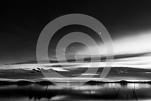 Beautiful view of Trasimeno lake Umbria, Italy at dusk, with black and white tones and moon in the sky