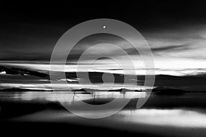 Beautiful view of Trasimeno lake Umbria, Italy at dusk, with black and white tones and moon in the sky