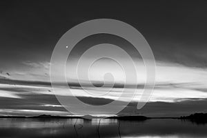 Beautiful view of Trasimeno lake Umbria, Italy at dusk, with black and white tones and moon in the sky