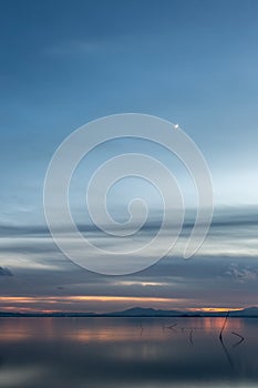 Beautiful view of Trasimeno lake Umbria, Italy at dusk, with blue and orange tones and moon in the sky