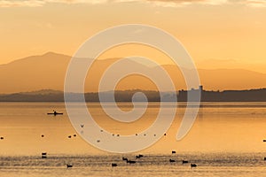 Beautiful view of Trasimeno lake Umbria, Italy at sunset, with orange tones, birds on water, a man on a canoe and