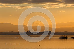 Beautiful view of Trasimeno lake Umbria, Italy at sunset, with orange tones, birds on water, a man on a canoe and