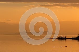 Beautiful view of Trasimeno lake Umbria, Italy at sunset, with orange tones, birds on water, a man on a canoe and