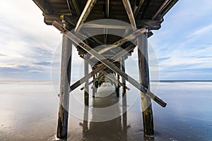 Beautiful view of the wet sand and bright sky from under the Myrtle Beach pier