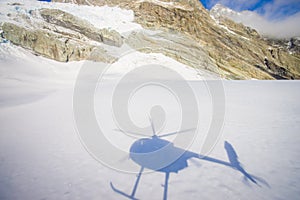 Beautiful view at white mountains covered with snow, with a helicopter shadow in the snow, in South Westland`s Southern